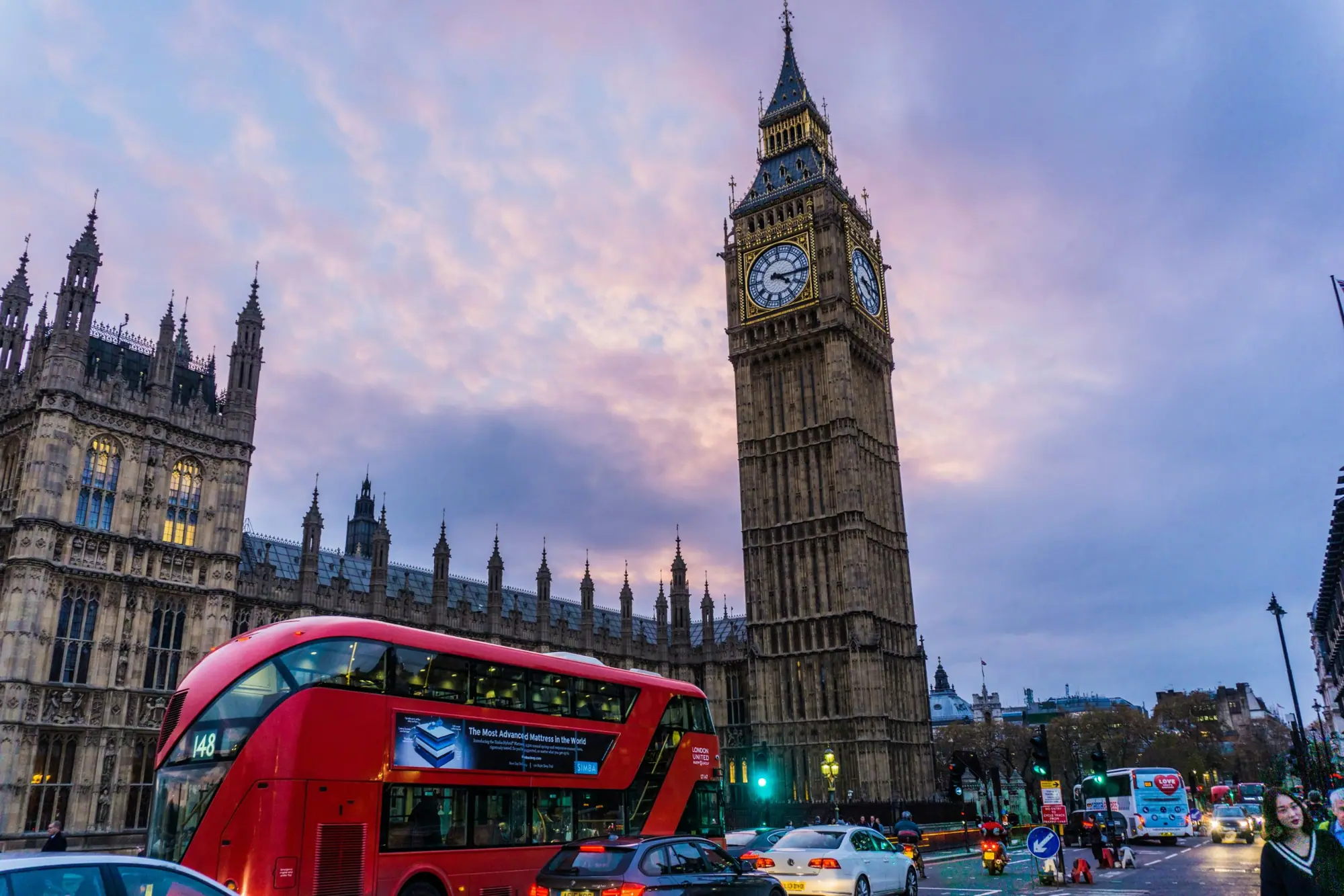 A red London bus passing Big Ben and the Houses of Parliament at dusk