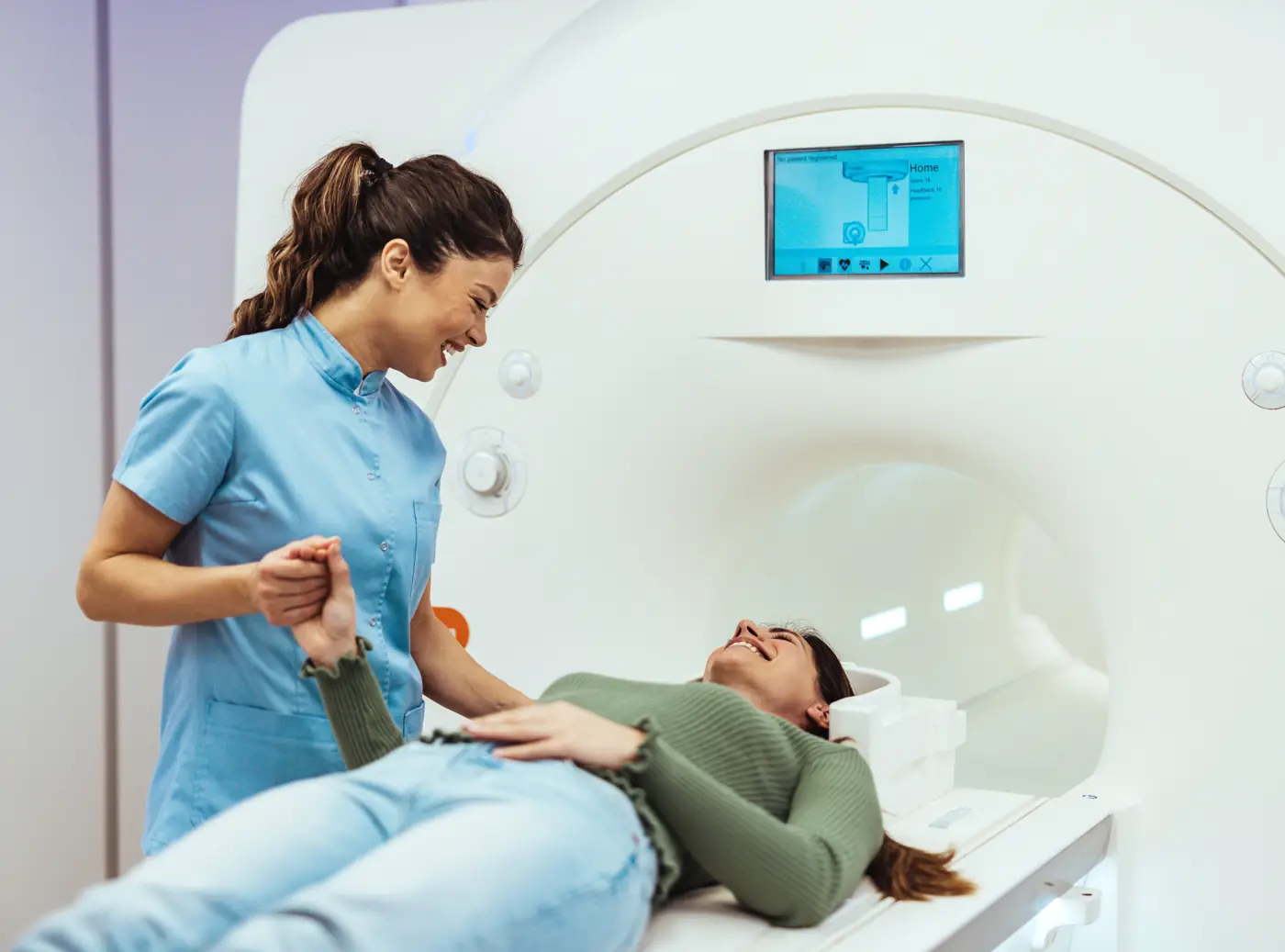 A smiling radiographer holding the hand of a patient lying on an MRI scanner table